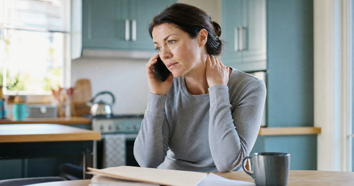 Woman on the phone with her auto insurer about PIP coverage after a car accident, rubbing a stiff neck, illustrating Maryland PIP and chiropractic care in Bowie, MD